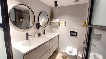 A modern bathroom with two sinks, a toilet, and a shower area.