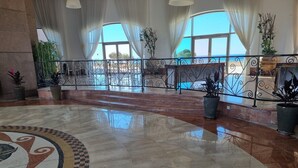 A spacious lobby with a polished marble floor, large windows with white curtains, and a metal railing overlooking a scenic view.