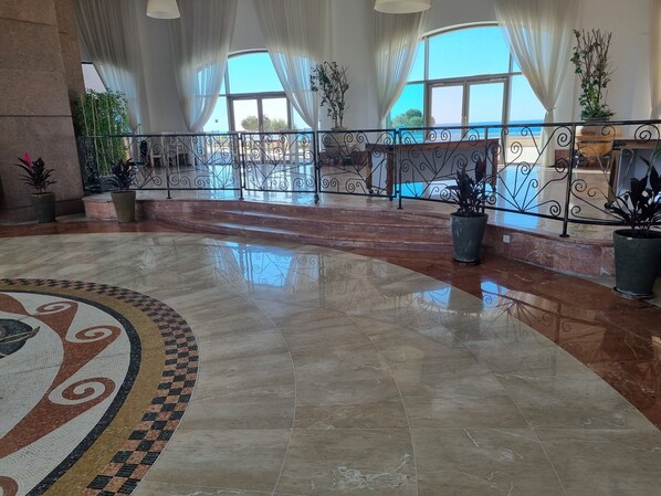 A spacious lobby with a polished marble floor, large windows with white curtains, and a metal railing overlooking a scenic view. - Sea Tower Almog (Haifa)