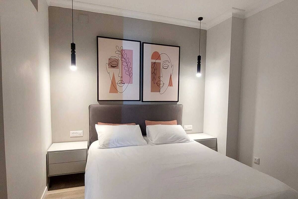 Une chambre moderne avec un grand lit, deux tables de chevet et deux lampes suspendues fixées au mur.