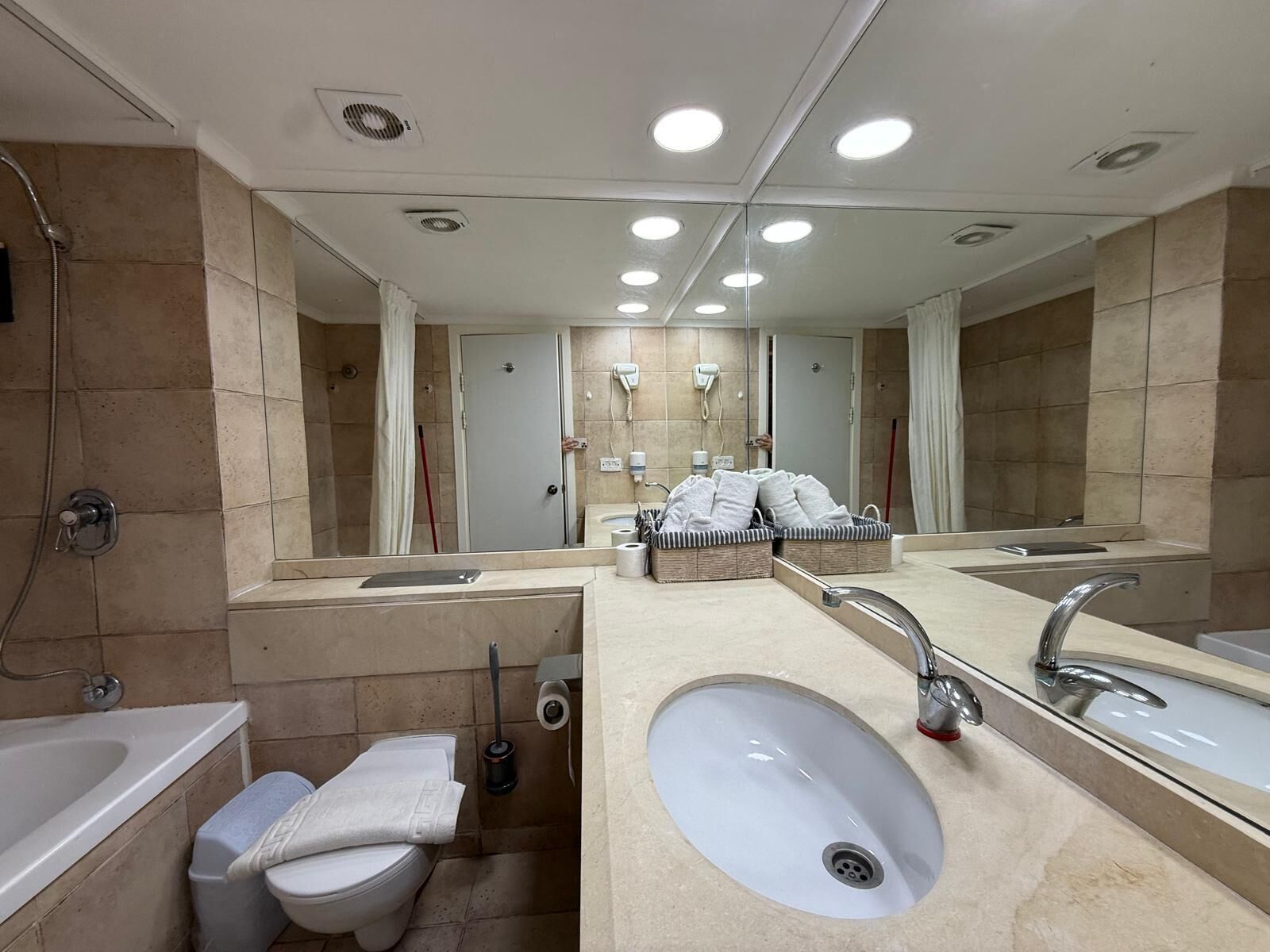 A modern bathroom with a large mirror, dual sinks, a toilet, and a shower.