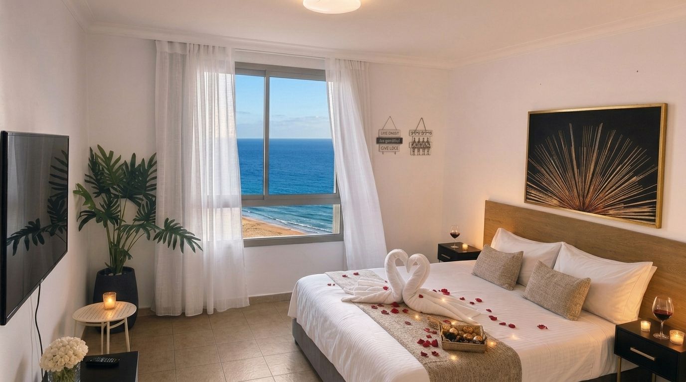A hotel room with a bed, a TV, a window with curtains, a plant, and a painting on the wall.