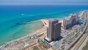A coastal cityscape with a prominent hotel featuring a modern design, situated near a beach and a busy road.