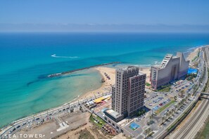 Un paysage urbain côtier avec un hôtel imposant à l’architecture moderne, situé près d’une plage et d’une route très fréquentée.