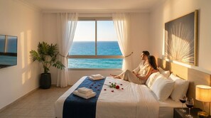 Habitación de hotel con una cama, vista al mar, planta en maceta y un cuadro en la pared.