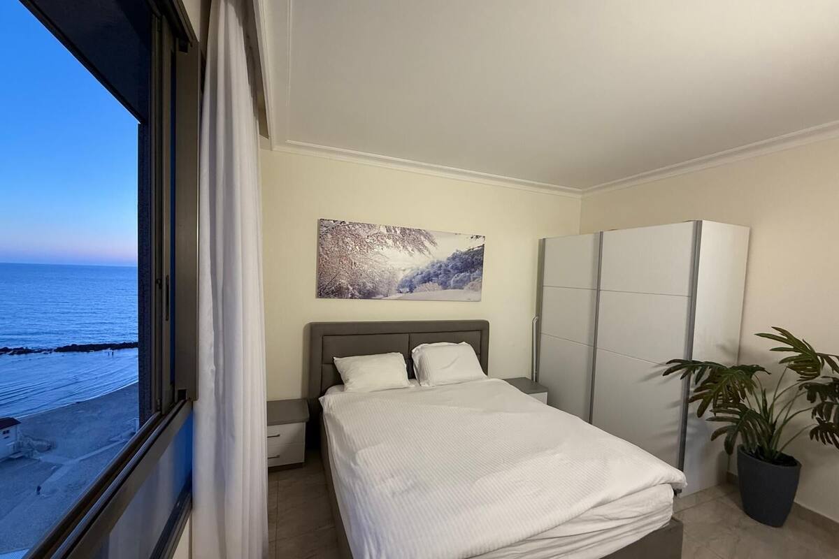 Une chambre à coucher comprenant un lit, une armoire, une table de chevet, une plante en pot et un tableau représentant un paysage enneigé.
