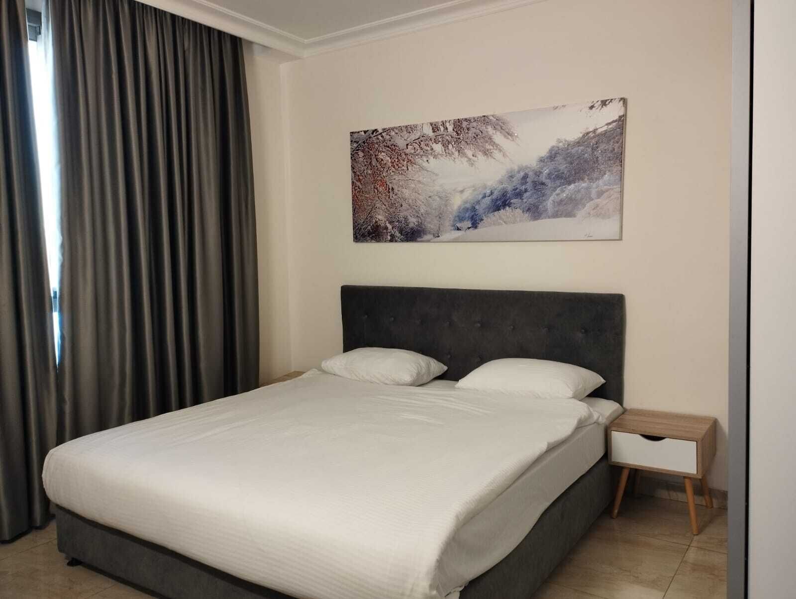 A modern hotel room with a large bed, a nightstand, and a painting on the wall.