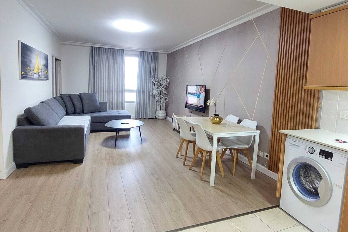 Un salon moderne avec un canapé gris, une petite table ronde et un téléviseur fixé au mur.
