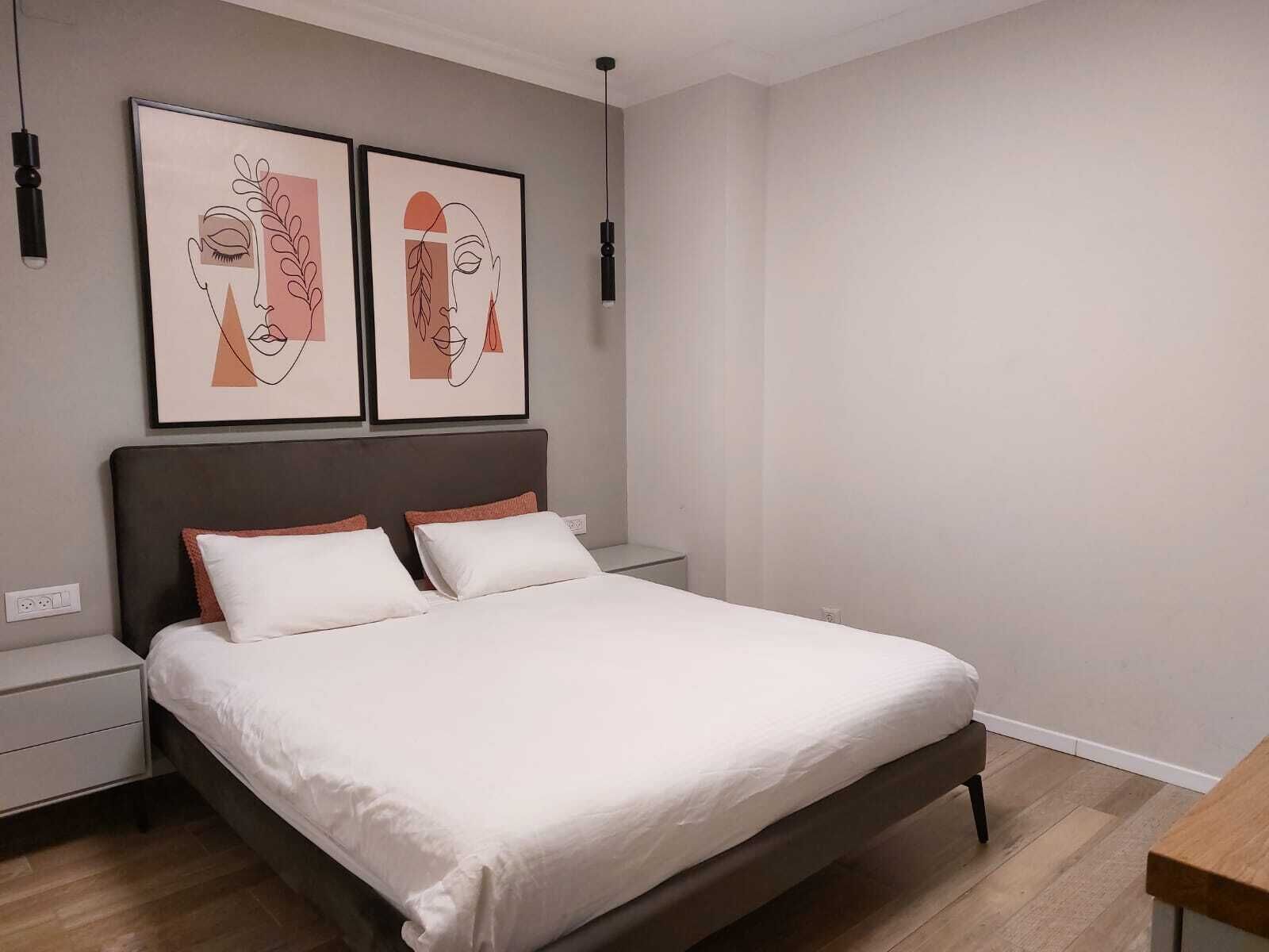 A modern bedroom with a large bed, two bedside tables, and two wall-mounted artworks.