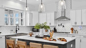 A modern kitchen with white cabinetry, a central island with bar stools, pendant lighting, and a view of the outdoors. - Lakefront Lake Anna - Decks, Views, Hot Tub (Louisa County)