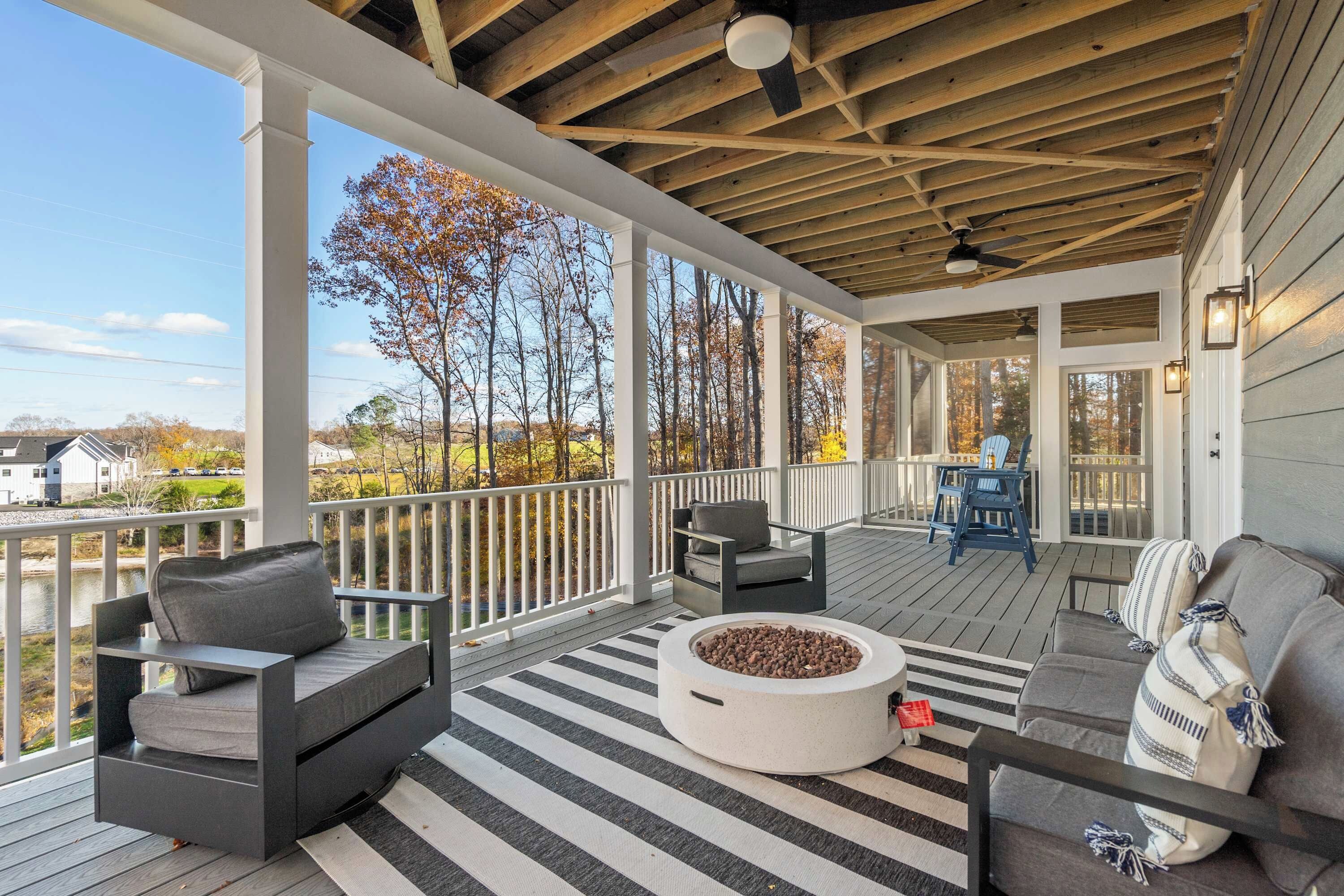 Lower Deck Fireside - Swivel chairs and a sofa surround the fire pit, with lake views through the trees and the neighborhood beyond.