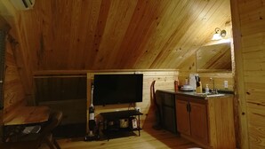 Un chalet en bois accueillant, doté d’un coin repas, d’une cuisine avec un évier et d’un téléviseur à écran plat fixé au mur.