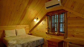 Une chambre mansardée chaleureuse, avec un lit, une petite commode, une fenêtre avec des volets et un appareil de climatisation.