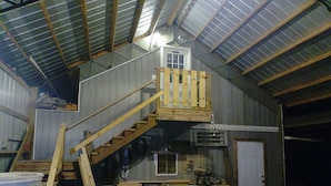 L’intérieur d’une grange rustique, avec un escalier en bois, une mezzanine et divers outils et équipements.