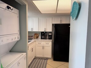 A compact kitchen with white cabinets, a black refrigerator, a coffee maker, and a microwave. - Cozy 2-bedroom 4 bed condo in Orange Beach directly across the street from Beach (Orange Beach)