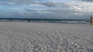 Een zandstrand met golven, een uitkijktoren voor de badmeester en een bewolkte lucht.