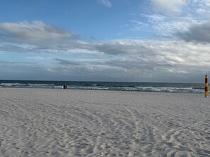 A sandy beach with waves, a lifeguard tower, and a cloudy sky. - Cozy 2-bedroom 4 bed condo in Orange Beach directly across the street from Beach (Orange Beach)