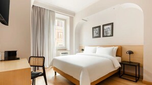 A hotel room with a bed, a desk, a chair, a nightstand, and two framed pictures on the wall. - The Couper Piazza di Spagna (Rome)