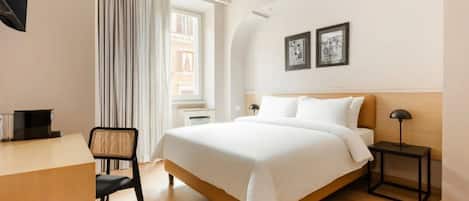 A hotel room with a bed, a desk, a chair, a nightstand, and two framed pictures on the wall.
