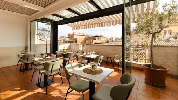 An outdoor dining area with multiple tables and chairs, large windows, and a view of the cityscape. - The Couper Piazza di Spagna (Rome)