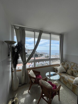 Ein Wohnzimmer mit Meerblick, einem runden Tisch, Korbstühlen, einer Couch und einer Stehlampe.