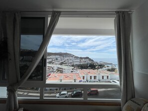 Ein Zimmer mit großem Fenster mit Blick auf eine Küstenstadt, das Gebäude und eine hügelige Landschaft zeigt.