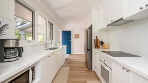Eine moderne Küche mit weißen Schränken, Edelstahlgeräten und einer blauen Tür im Hintergrund.