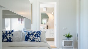Ein Schlafzimmer mit einem Bett, einem Nachttisch mit Pflanze und Blick ins Badezimmer.