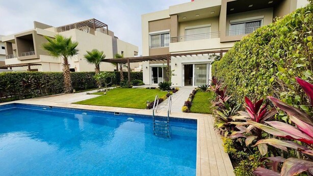 A modern hotel with a swimming pool, a well-maintained garden, and a covered outdoor area. - فيلا للايجار اليومي خمس غرف داخل كمبوند بالم هيلز
villa for daily rent (Giza Governorate)