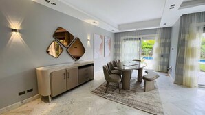 A modern dining area with a round table, chairs, and a bench. There are wall-mounted mirrors and artwork. - فيلا للايجار اليومي خمس غرف داخل كمبوند بالم هيلز
villa for daily rent (Giza Governorate)