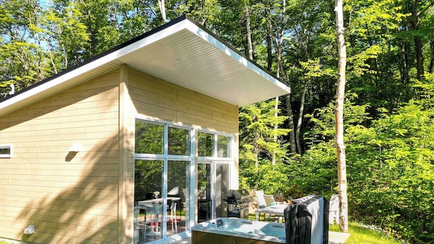 Une petite cabane avec une porte en verre, un jacuzzi et un barbecue à l’extérieur.