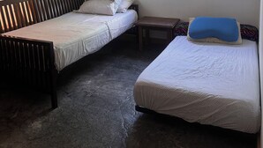 Enkel indkvartering i et lille rum med to enkeltsenge, en loftsvifte, et vindue med let gardin og et lille bord.