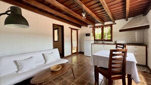 Une pièce chaleureuse avec un canapé blanc, une petite table et une table à manger en bois, ainsi que des chaises. On y trouve également un coin cuisine équipé d’une cuisinière et d’un four à micro-ondes.