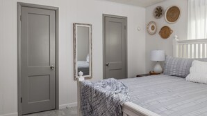 Une chambre avec deux portes, un lit recouvert d’une couette grise, une lampe de chevet et des éléments de décoration murale en fibres tressées.