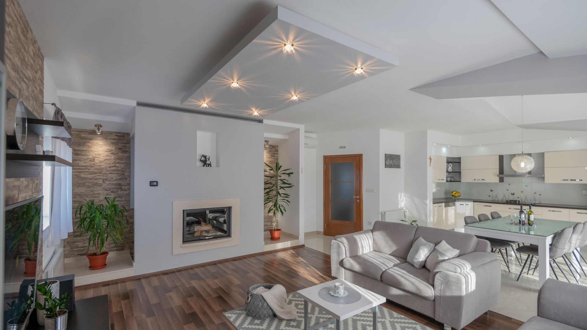 Un salon moderne avec un canapé, une table basse et une cheminée. On y trouve également un coin repas avec une table et des chaises, et une cuisine à l’arrière-plan.