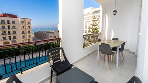 Een balkon met zwembad, een eethoek met tafel en stoelen, en uitzicht op zee en gebouwen.