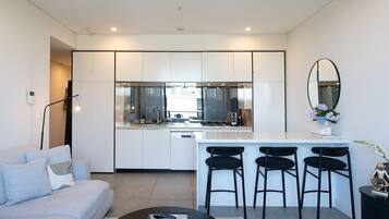A modern kitchen with white cabinets, a central island with bar stools, a large mirror, and a dining area with a sofa and coffee table.