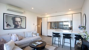 A modern living room with a sofa, coffee table, and a kitchen area with a bar and chairs. - Riverside Parramatta I90 (Parramatta)