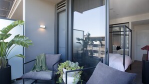 A modern hotel room with a balcony, a bed, a seating area with cushions, and a potted plant. - Riverside Parramatta I90 (Parramatta)