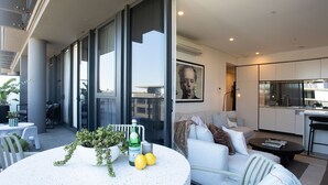 A modern living room with a round table, a sofa, and a kitchen area with a large window. - Riverside Parramatta I90 (Parramatta)