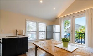 A kitchen with a sink, cabinets, and a countertop. There are two windows with blinds, a refrigerator, and a balcony with a railing.