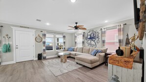 A living room with a beige sectional sofa, a round coffee table, and a ceiling fan. - Pirate's Bay. New build! Pets! Hot Tub! Affordable! Views of Ocean AND Bay! (Surfside Beach)