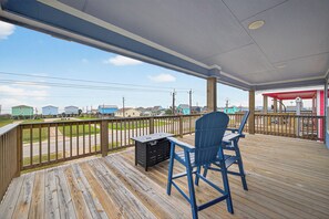 A covered outdoor deck with a wooden floor, a blue chair, and a small table. - Pirate's Bay. New build! Pets! Hot Tub! Affordable! Views of Ocean AND Bay! (Surfside Beach)