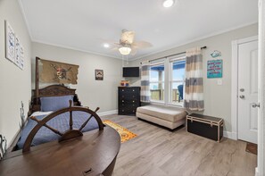 A bedroom with a bed, a wooden table, a ceiling fan, a dresser, a window with curtains, and a door. - Pirate's Bay. New build! Pets! Hot Tub! Affordable! Views of Ocean AND Bay! (Surfside Beach)
