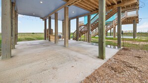 A covered outdoor area with wooden beams and concrete flooring, featuring a staircase leading to an upper level. - Pirate's Bay. New build! Pets! Hot Tub! Affordable! Views of Ocean AND Bay! (Surfside Beach)