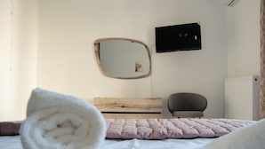 Un dormitorio con cabecera de madera, cama con colcha rosa, manta blanca, espejo redondo y altavoz negro en la pared.