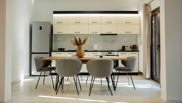 Una cocina moderna con armarios blancos, una mesa de comedor de madera y cuatro sillas grises.