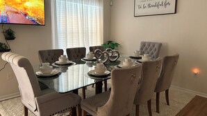 Comedor con mesa de vidrio, seis sillas tapizadas y una cita enmarcada en la pared.