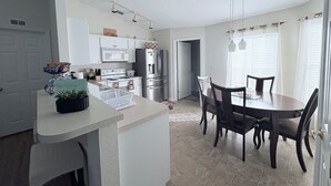 Una cocina moderna con armarios blancos, electrodomésticos de acero inoxidable y una zona de comedor con una mesa y sillas de madera oscura.
