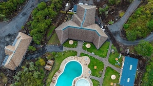 An aerial view of a property with a swimming pool, a large building with a unique roof design, and a smaller structure to the left. - Sleeping Warrior Camp Elementaita (Gilgil)